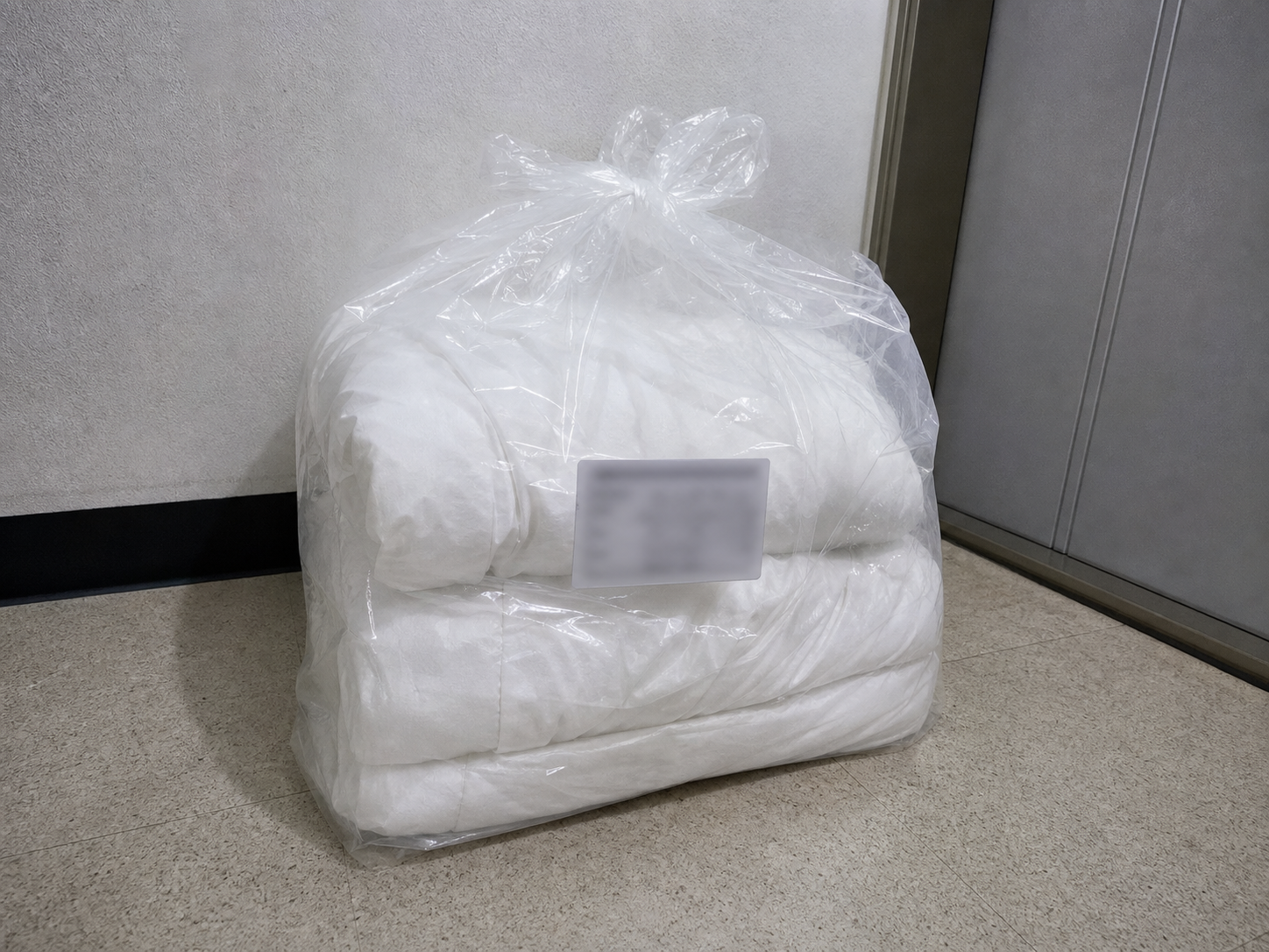 현관 앞 투명 비닐 봉투 안에 접힌 흰 이불 커버